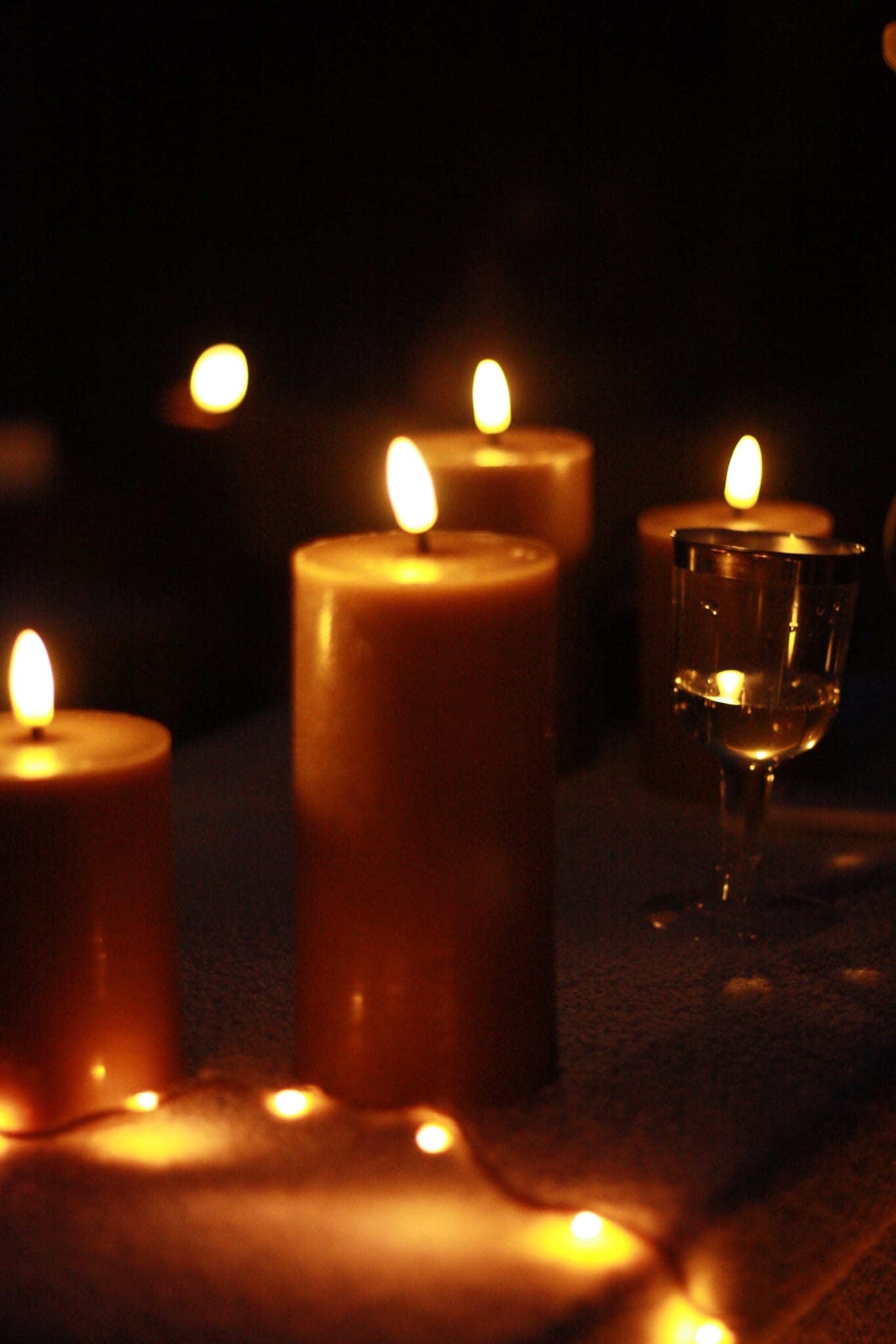 Bougies allumées, guirlande lumineuse et verre de vin blanc créant une ambiance cosy